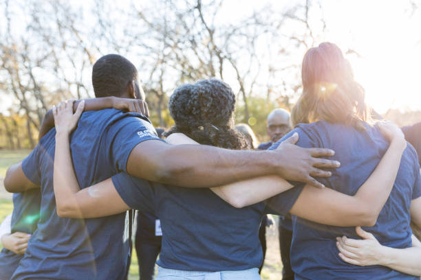 Group of diverse neighbours are unified while participating in a community clean-up event. They are standing with their arms around one another.